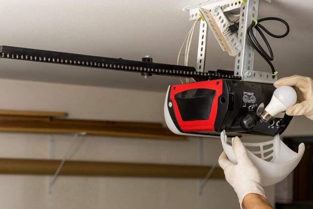 The Complete Guide to Garage Door Opener Repair in Maine – What You Need to Know 1 Technician performing a garage door opener repair, replacing the light bulb and inspecting the motor housing for proper functionality.